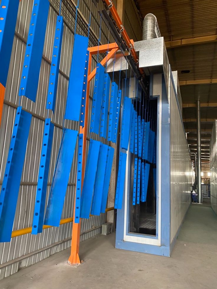 Pièces métalliques bleues suspendues à un convoyeur aérien entrant dans un four de thermolaquage