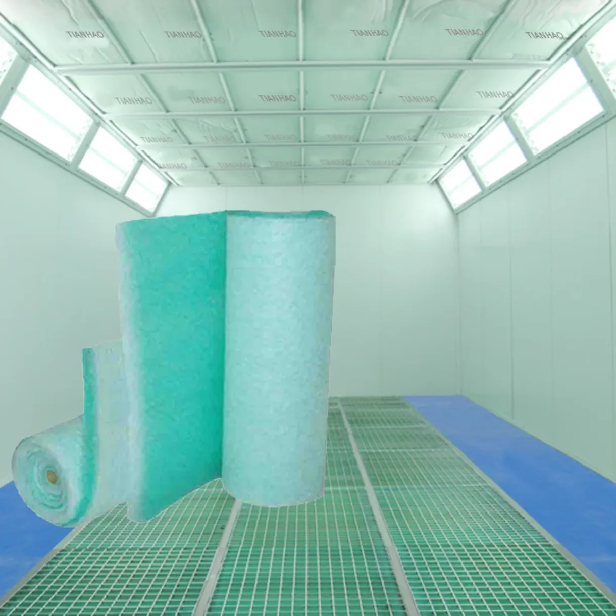 Rouleau de média filtrant vert pour sol devant une cabine de peinture industrielle éclairée.