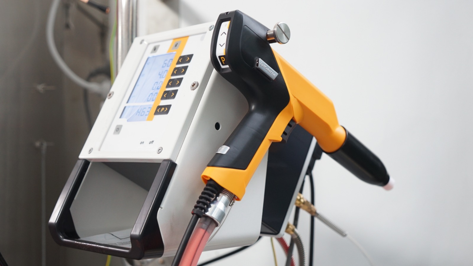 Pistolet de thermolaquage électrostatique jaune et noir posé sur son boîtier de commande digital.
